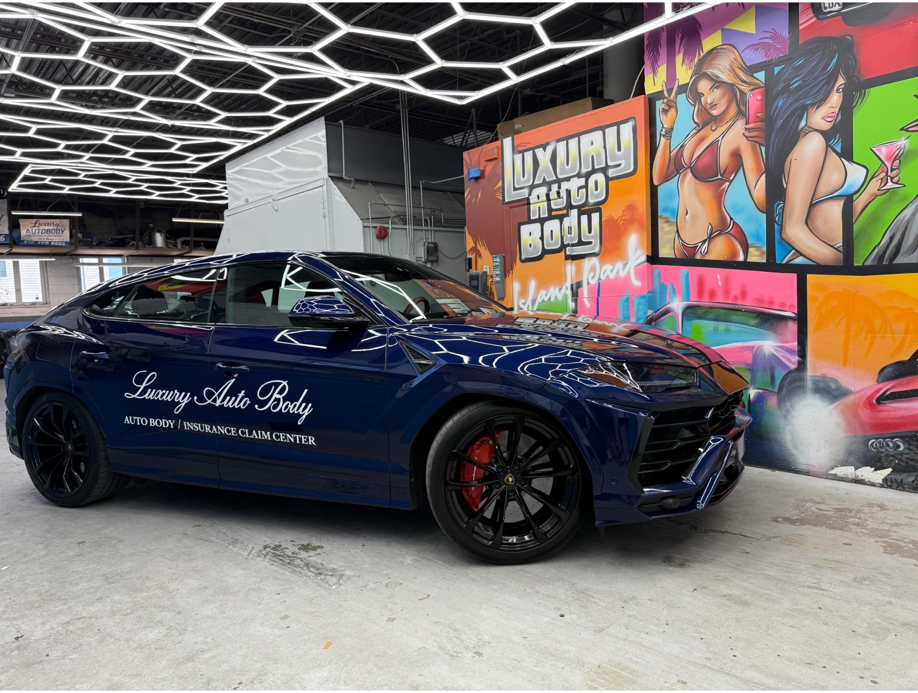Lamborghini Urus wrapped with Luxury Auto Body branding inside the shop under hexagon lighting